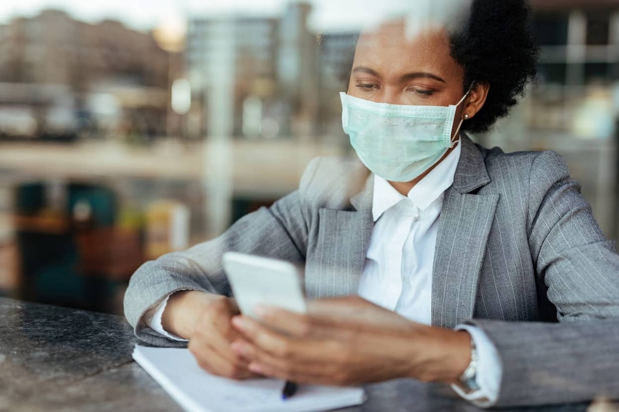 looking through a window at a person wearing mask holding a cell phone