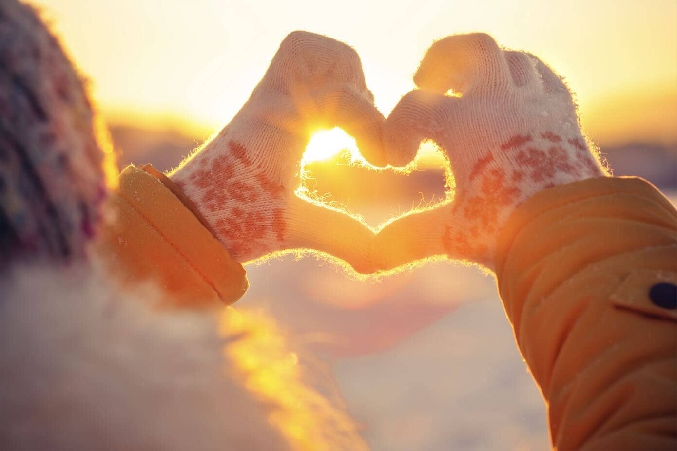 person with winter gloves making a heart with hands with the sun glowing