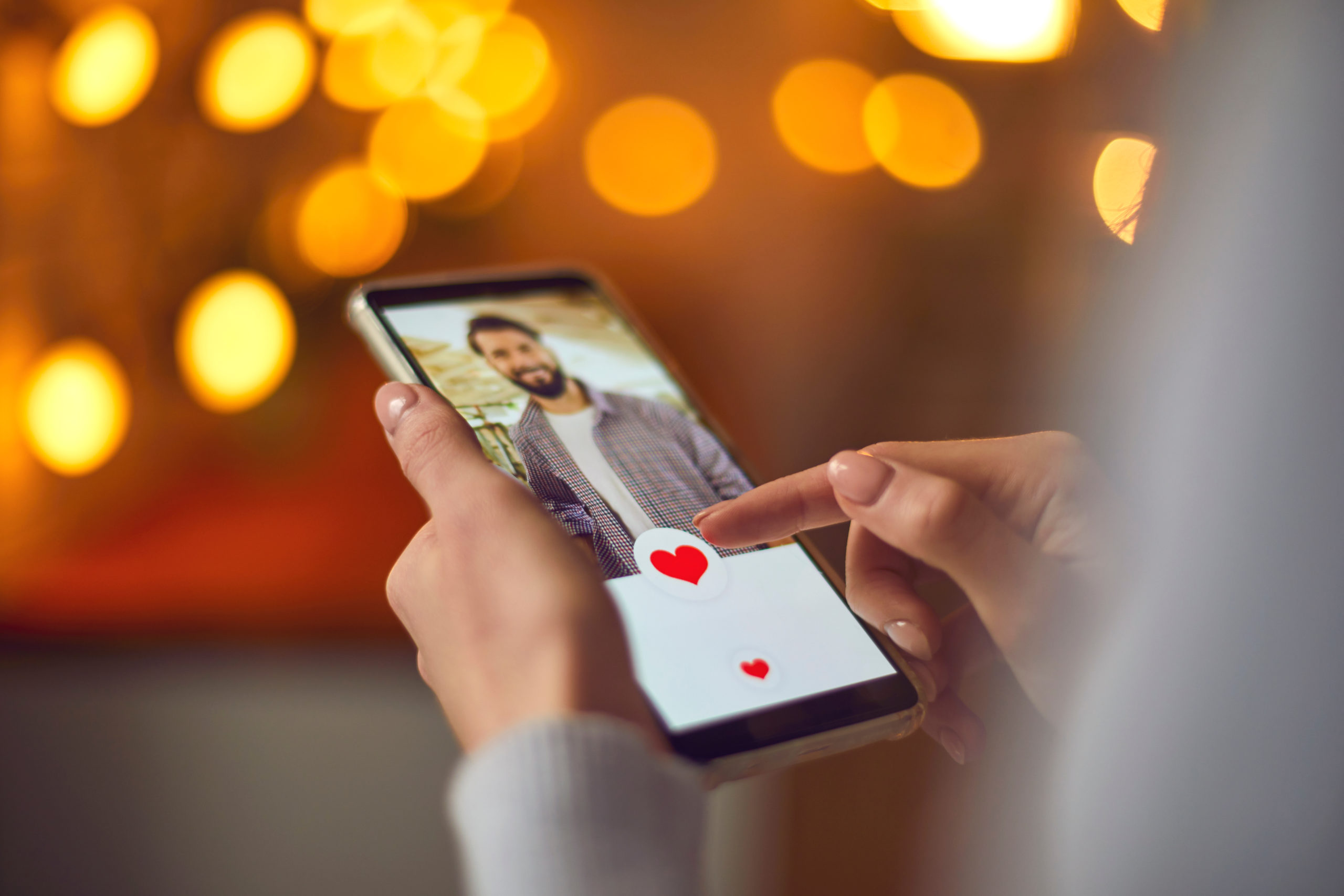 Woman looking at attractive young man's profile photo on dating app and pressing red heart like button