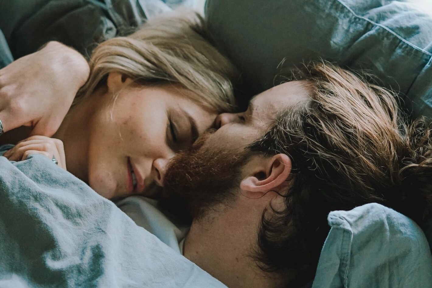 man kissing woman on forehead while lying in bed