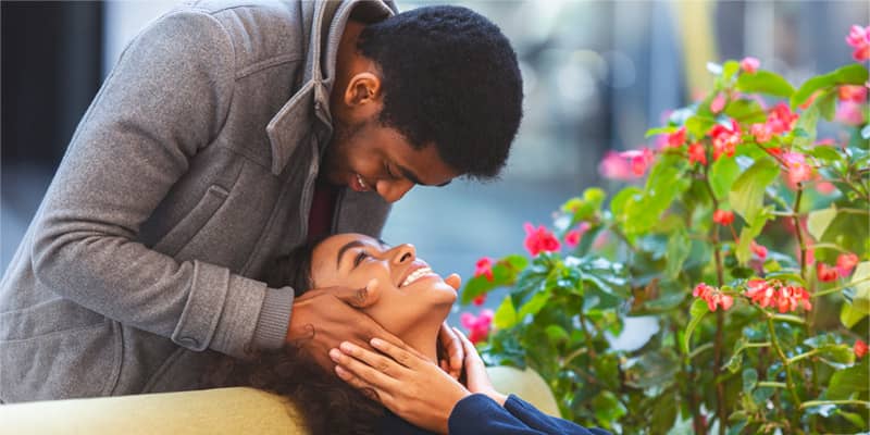 Man staying behind woman and touching her face, looking at her eyes