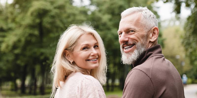 Smiling happy spouse embracing while walking on a date in park together.